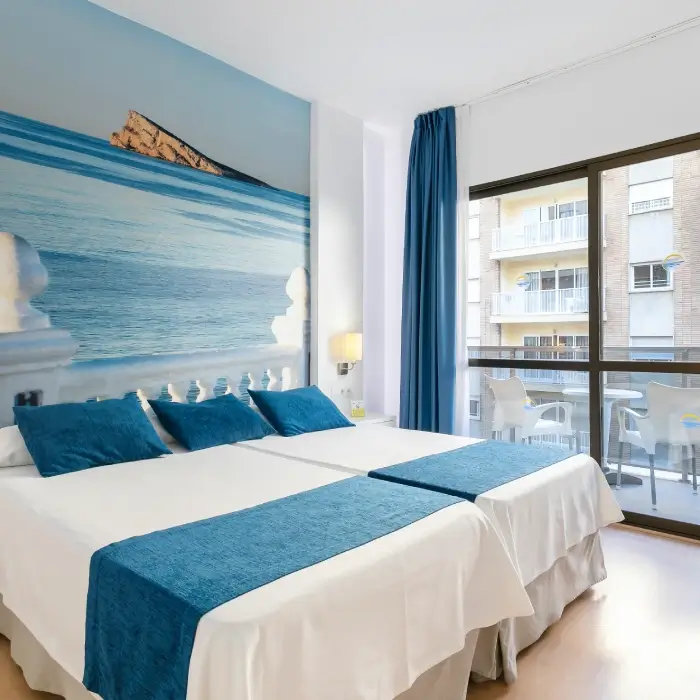 Habitación con dos camas, mural de mar, ventana y cortinas azules.
