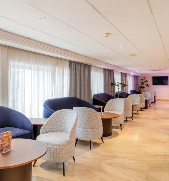 Sala de espera con sillones grises y mesas circulares frente a ventanales.