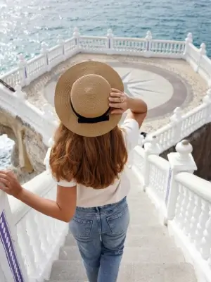 Mujer con sombrero sube escaleras hacia mirador con vista al mar.