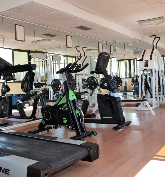 Gimnasio con bicicletas estáticas, cinta de correr y espejos en la pared.