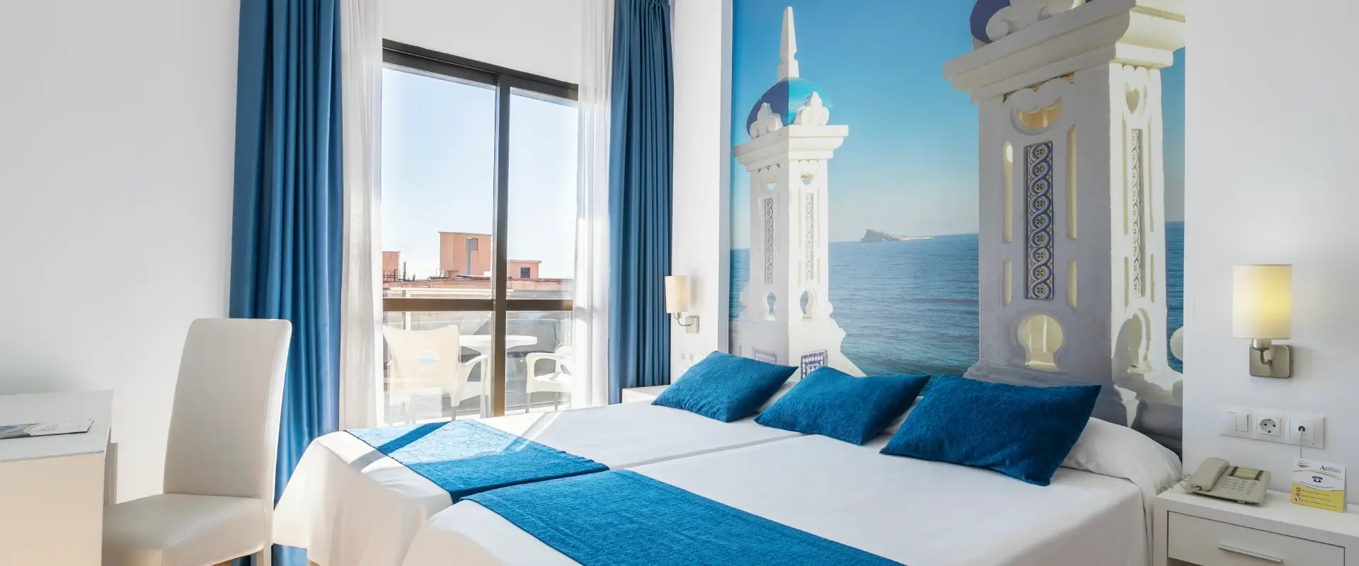 Habitación luminosa con cama doble, ventanas amplias y mural del mar.