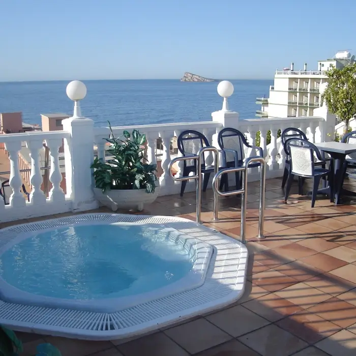 Jacuzzi en terraza con vista al mar y sillas alrededor.