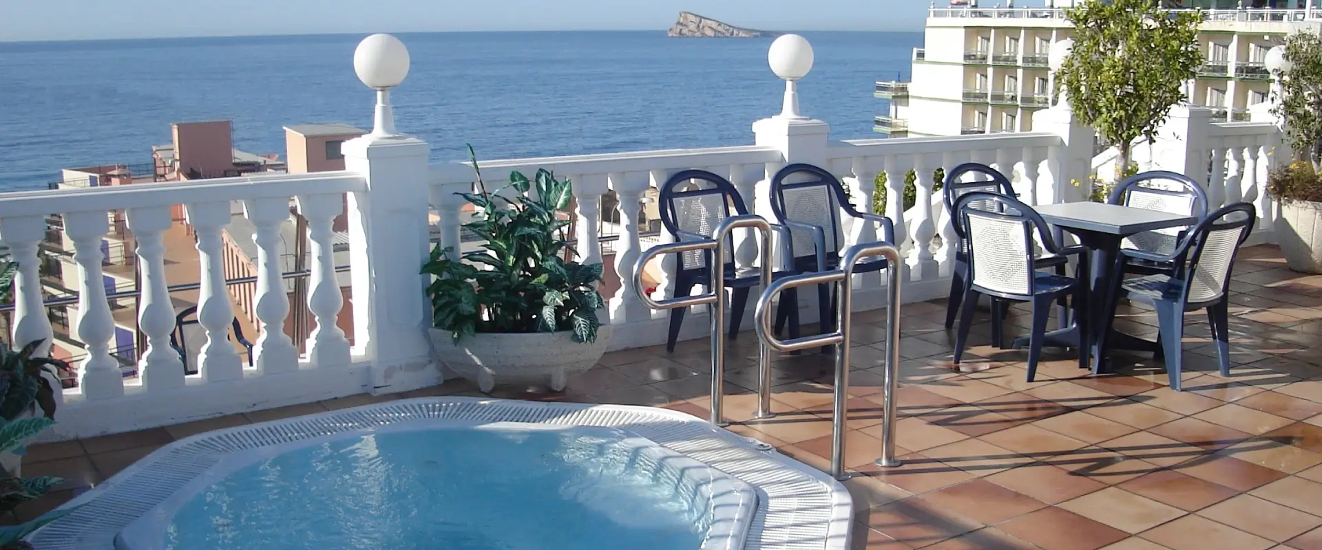 Terraza con jacuzzi, sillas y vista al mar en un día soleado.