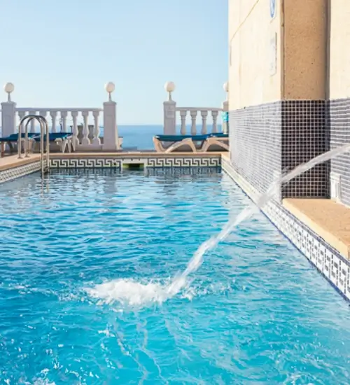 Piscina con caño de agua y vista al mar al fondo.