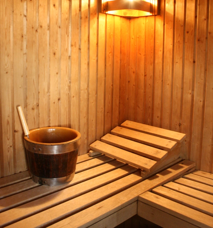 Sauna de madera con un balde y un asiento inclinado iluminado suavemente.
