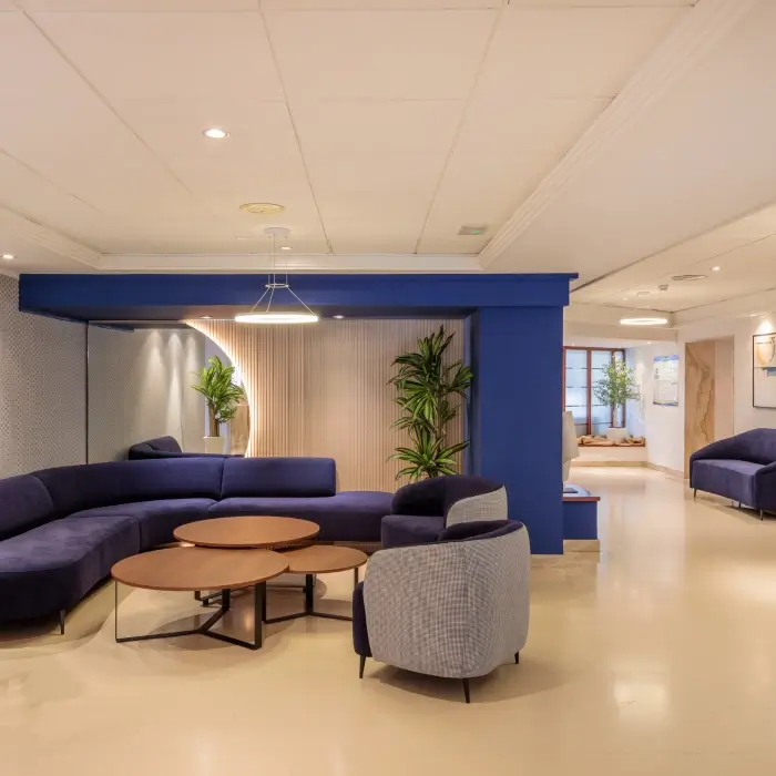 Sala moderna con sofás azules, mesas redondas y plantas decorativas.