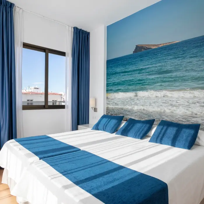Habitación luminosa con cama, sábanas azules y mural de playa.