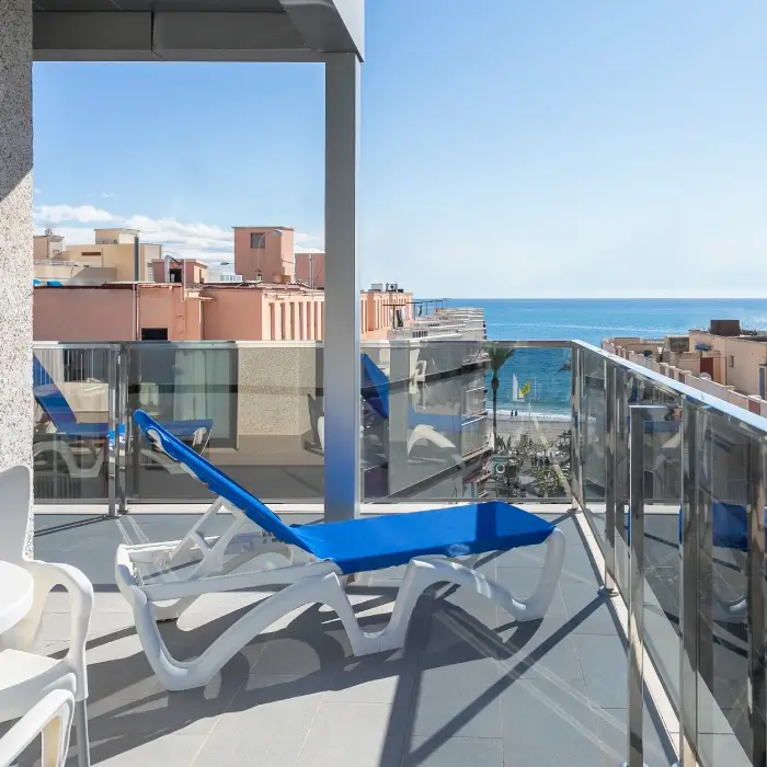 Terraza con tumbonas azules y vista al mar y edificios cercanos.