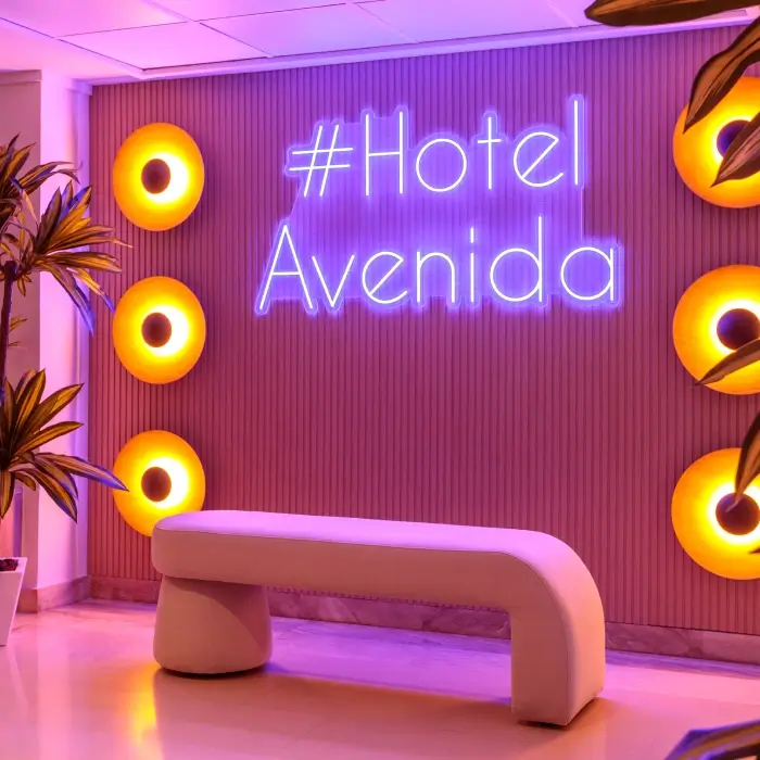 Sala iluminada con neón "#Hotel Avenida" y decoraciones circulares naranjas.
