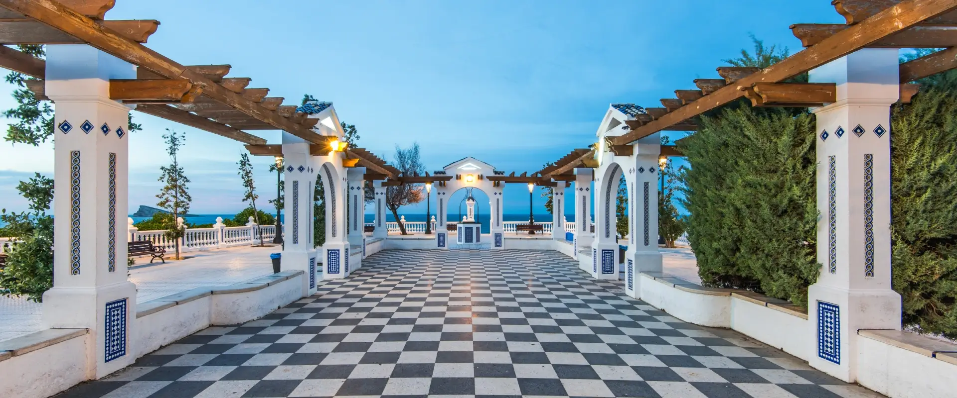 Terraza con suelo ajedrezado, arcos blancos y vista al mar.