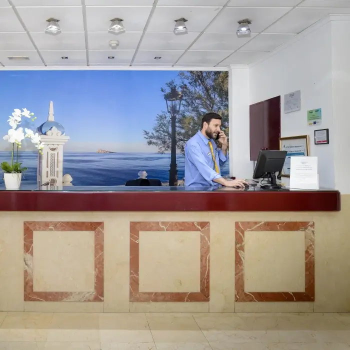 Recepcionista hablando por teléfono en un mostrador de hotel con fondo de paisaje.