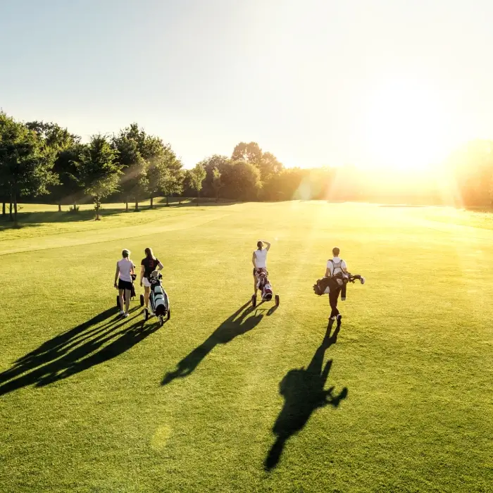 Cuatro personas caminando en un campo de golf al atardecer.