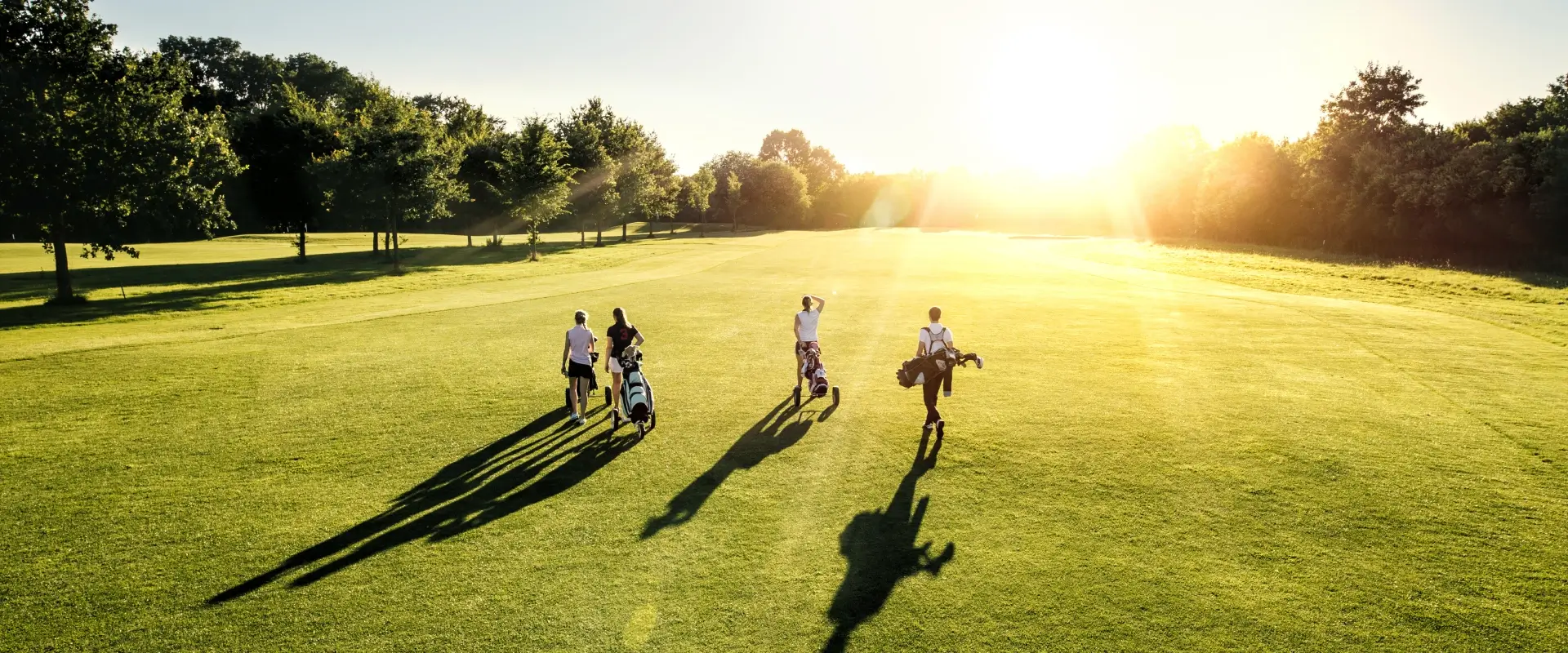 Cuatro personas caminando al atardecer en un campo de golf.