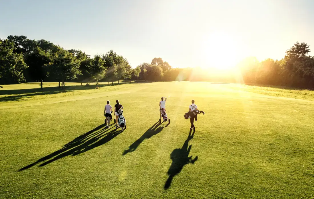 Jugadores de golf caminan al atardecer por un campo verde y soleado.