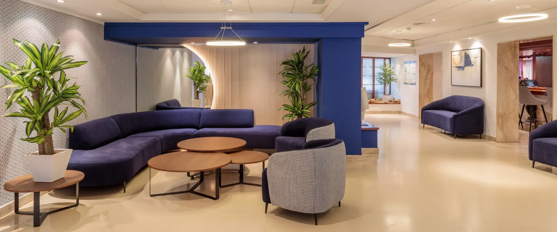 Sala moderna con sofás azules, plantas y mesas de centro redondas.