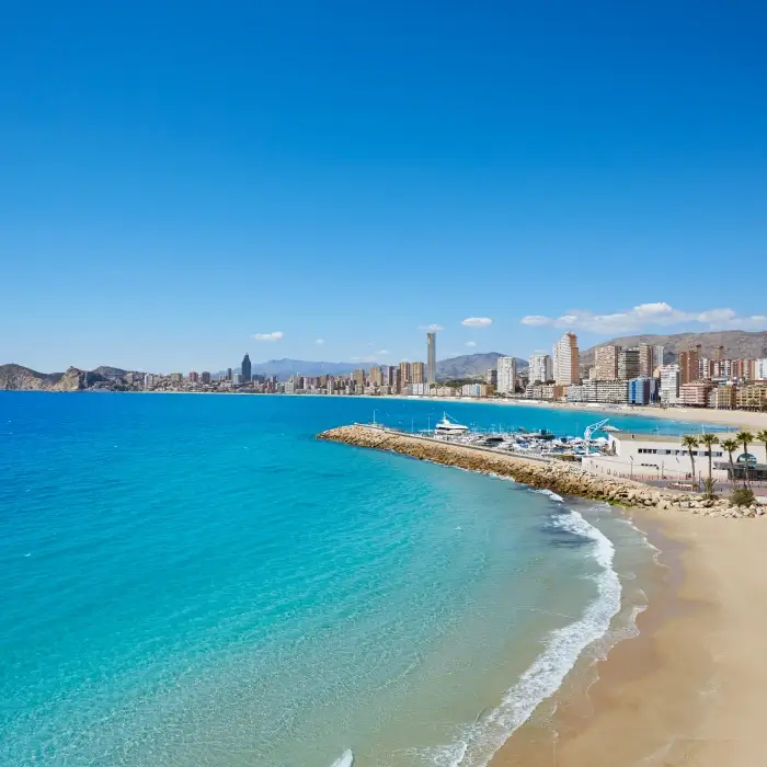Playa con edificios al fondo bajo un cielo azul despejado.