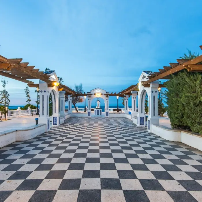 Terraza con patrón de tablero de ajedrez y arcos; vista al mar al fondo.
