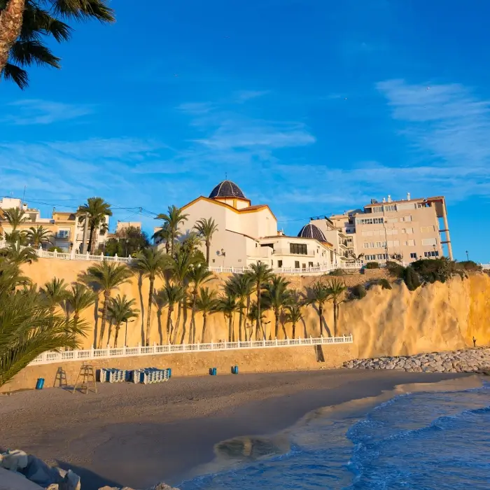 Playa con palmeras, edificios y cielo azul al fondo.