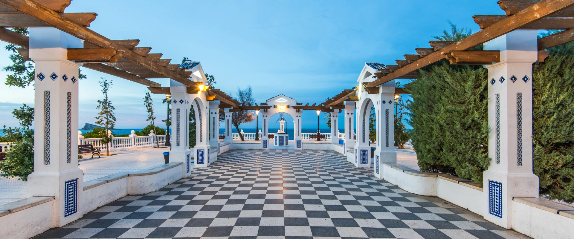 Terraza con suelo ajedrezado, vista al mar y estructura de arcos blancos.