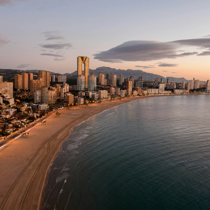 Ciudad costera al atardecer con edificios altos y playa tranquila.