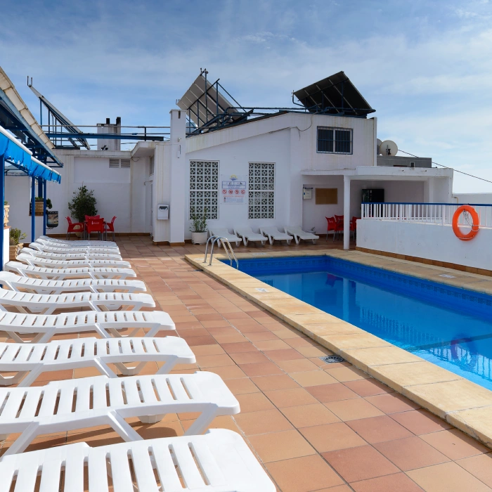 Piscina en una terraza con varias tumbonas blancas y cielo despejado.