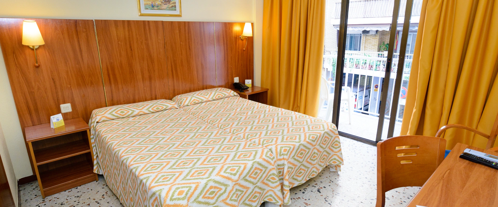 Habitación con cama doble, cortinas amarillas y balcón con vista exterior.