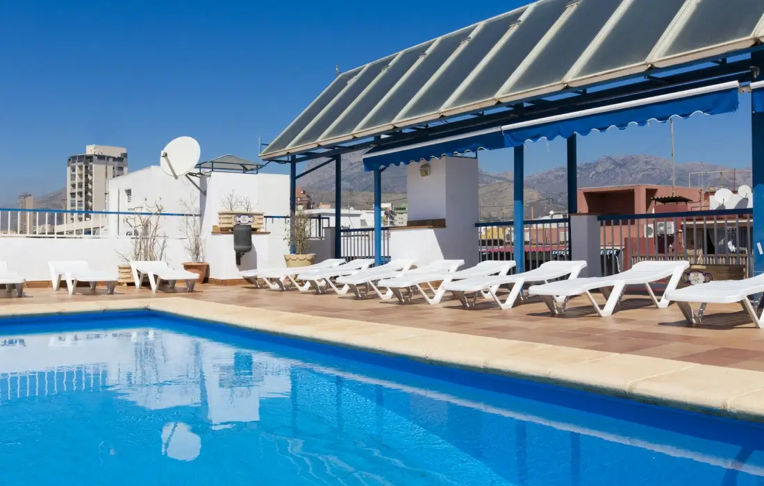 Piscina en la azotea con sillas blancas y vista a edificios lejanos.