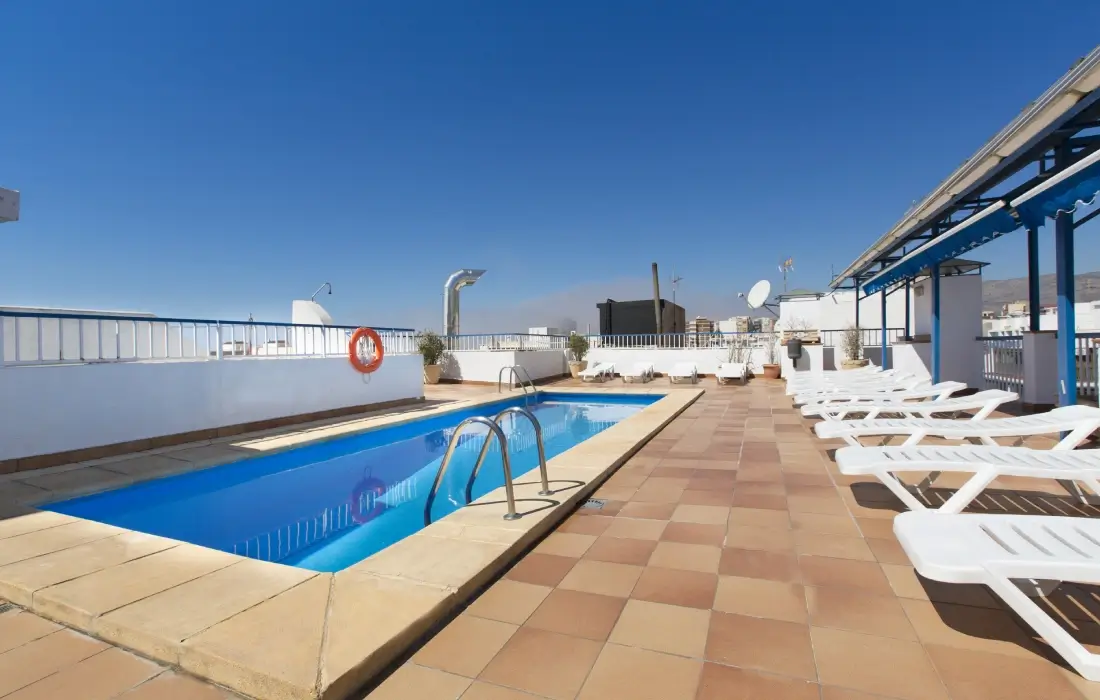Piscina en azotea con tumbonas blancas y cielo despejado.