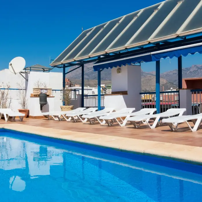 Piscina en azotea con tumbonas y estructura azul bajo cielo despejado.
