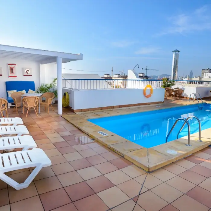 Piscina en azotea con tumbonas y sillas bajo un cielo azul.