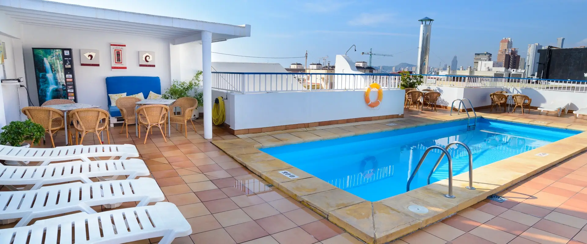 Terraza con piscina, sillas y mesas de mimbre bajo un cielo despejado.