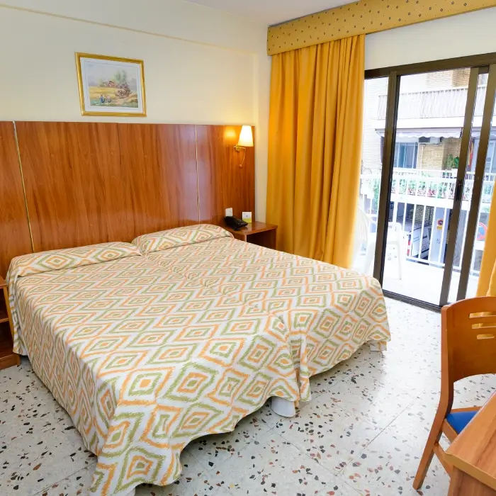 Habitación de hotel con cama doble, cortinas amarillas y balcón.