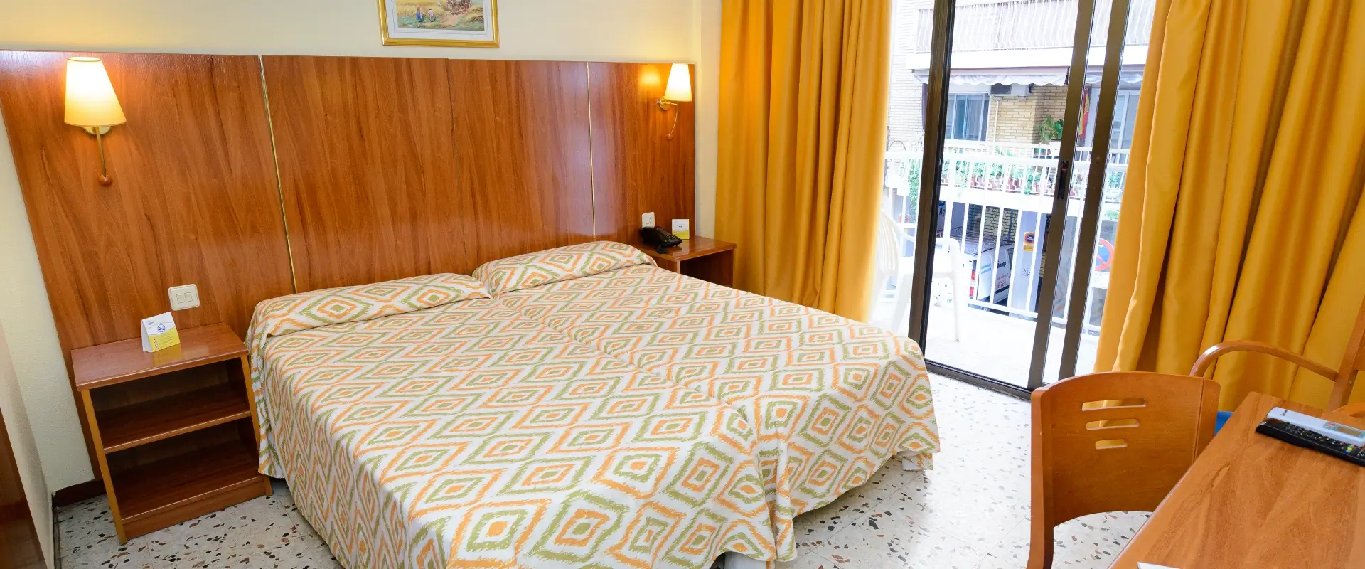 Habitación con cama doble, cortinas amarillas y puerta a balcón.