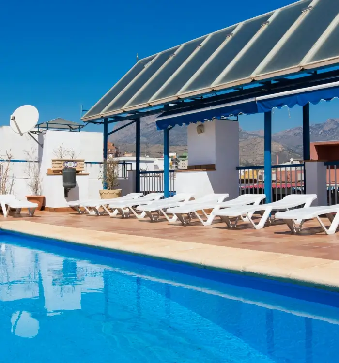 Piscina al aire libre con tumbonas y montañas al fondo.