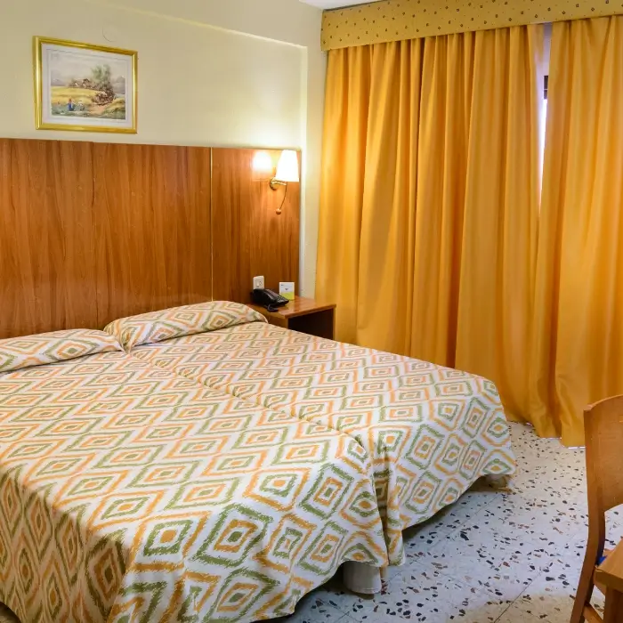 Habitación de hotel con cama doble y cortinas amarillas.