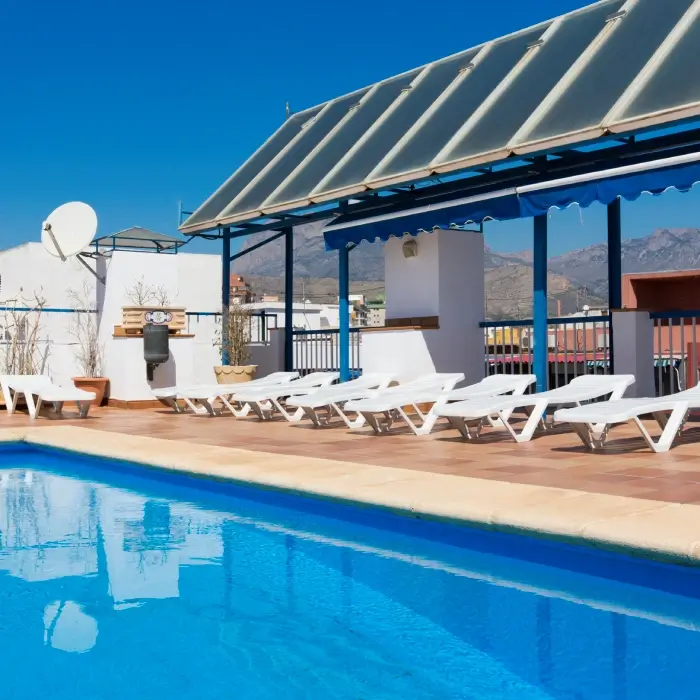 Piscina en azotea con tumbonas y montañas al fondo.