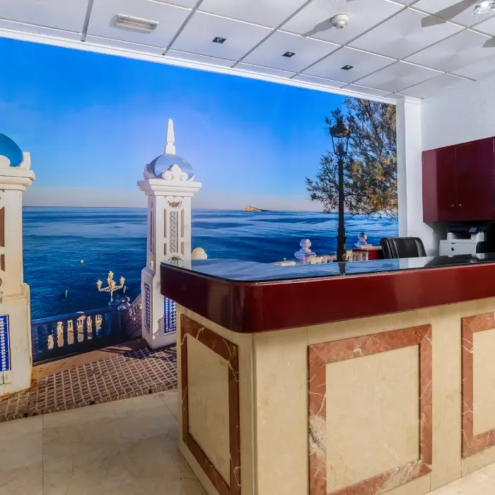 Mostrador de recepción con fondo de un mural de paisaje costero al atardecer.