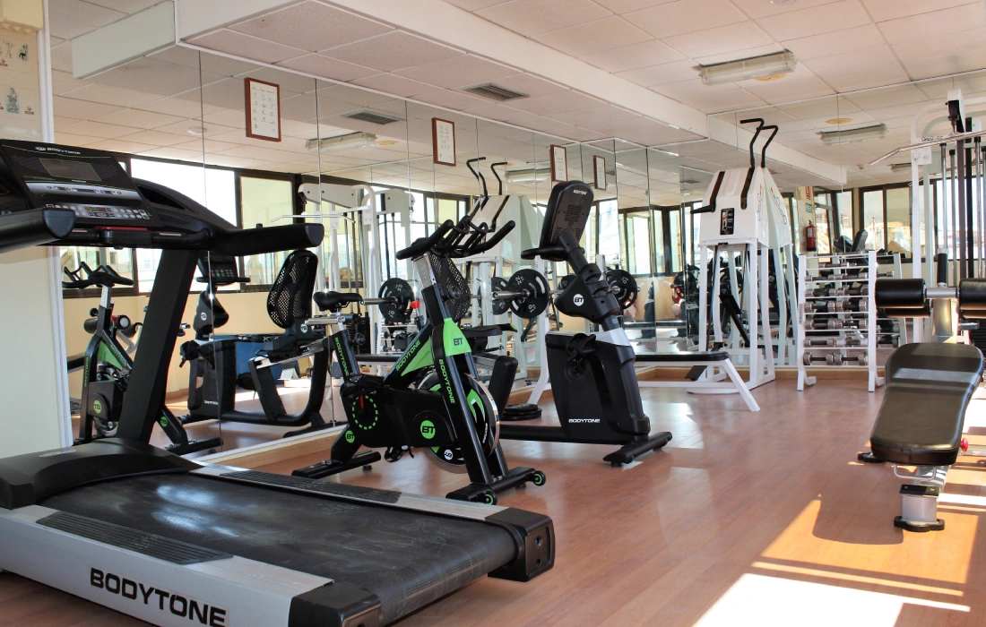 Gimnasio con máquinas de ejercicio y grandes espejos iluminado por la luz natural.