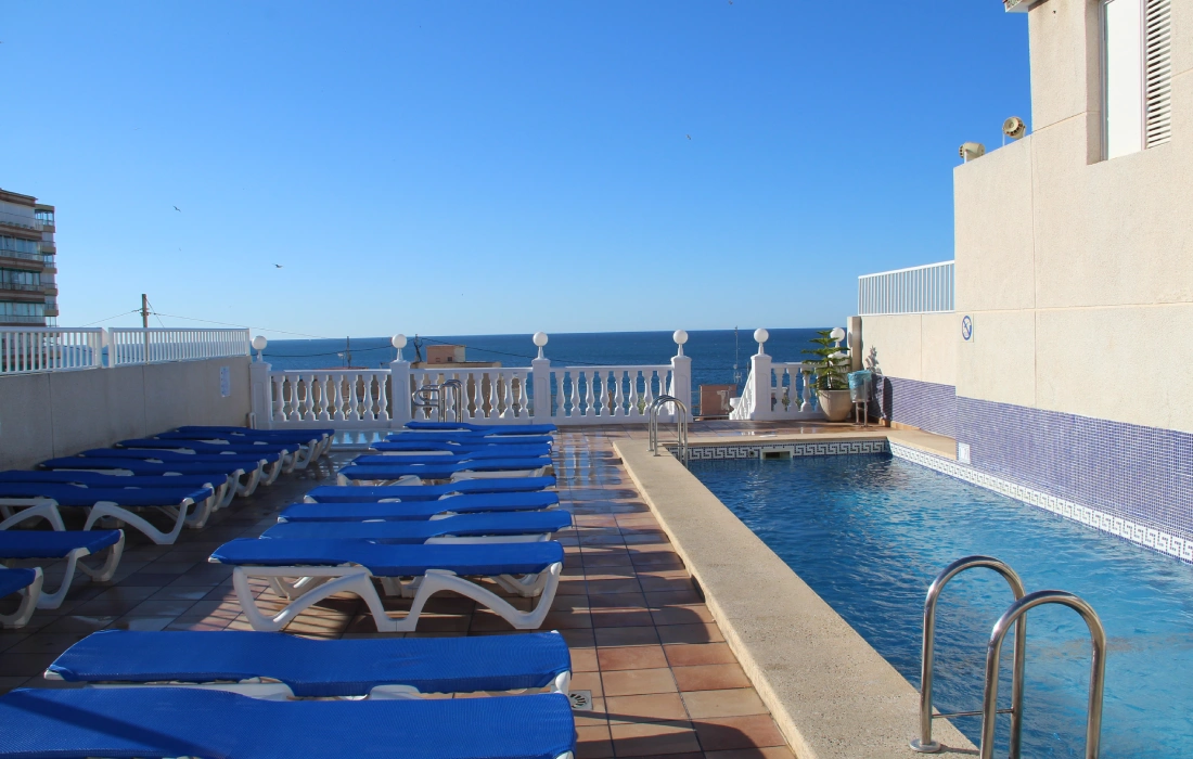 Piscina junto a camastros azules con vista al mar.