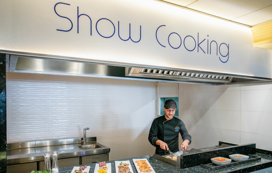 Chef preparando comida en una estación de cocina en vivo bajo un letrero.