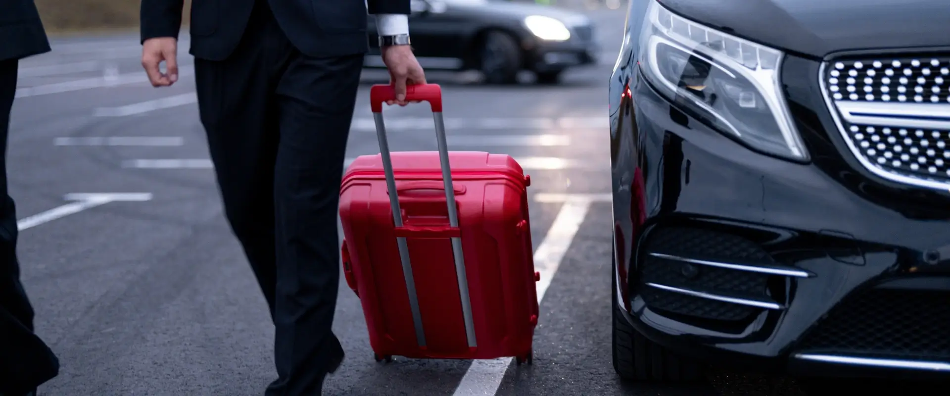 Hombre con maleta roja caminando junto a un coche negro.