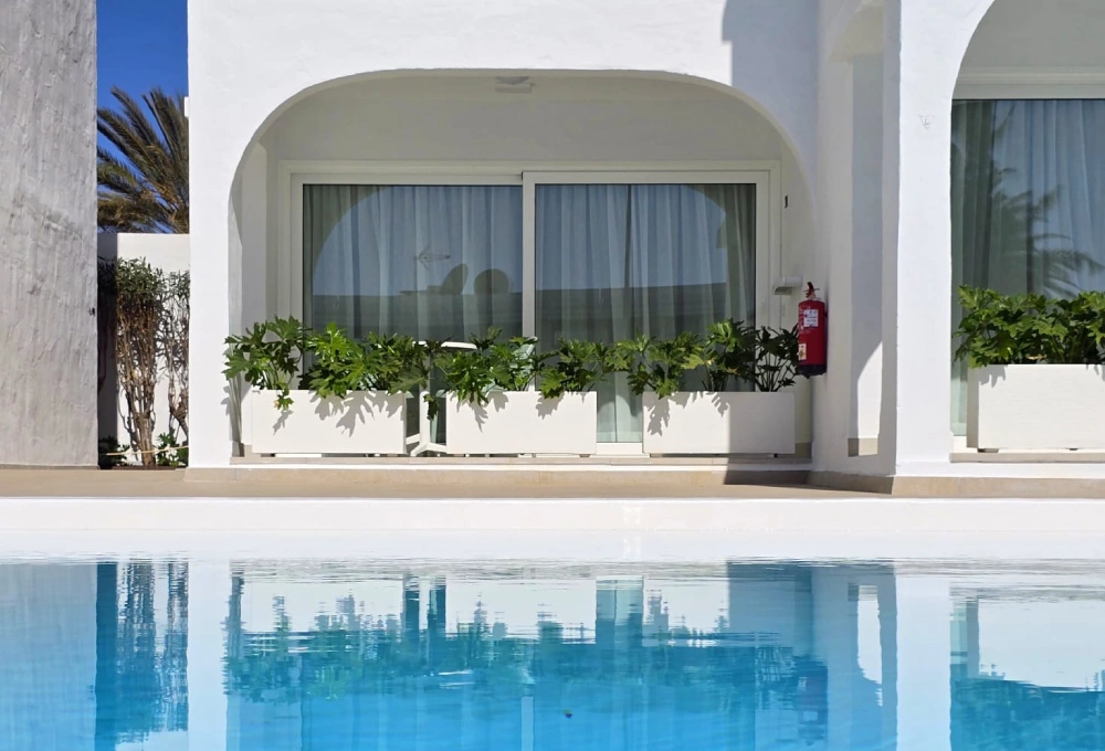 Edificio blanco con plantas y piscina reflectante.