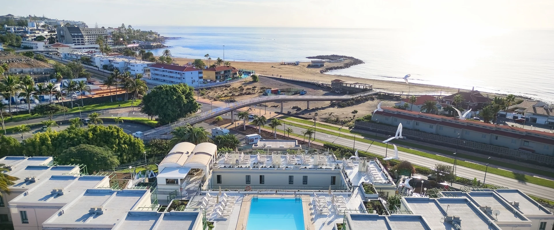 Vista a&eacute;rea de un complejo hotelero con piscina y una playa al fondo, bajo el cielo despejado.