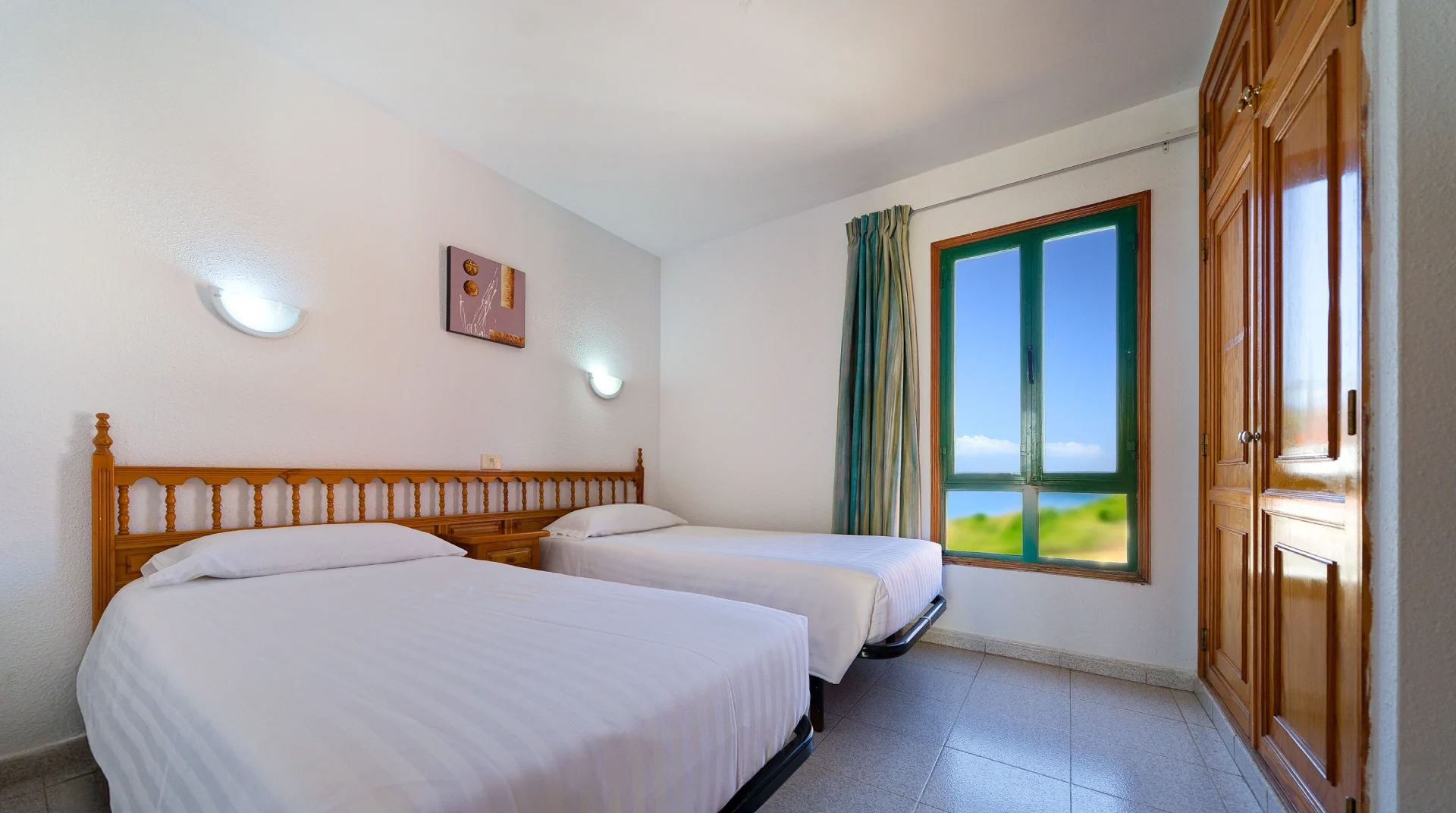 Habitaci&oacute;n con dos camas individuales, ventana con vista al mar y muebles de madera.