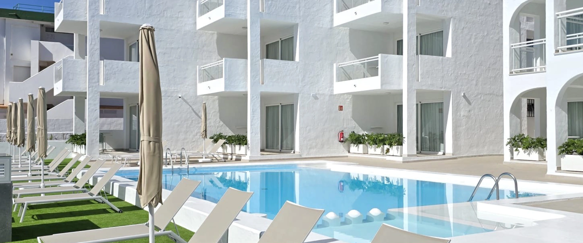 Piscina al aire libre con sillas reclinables y edificio blanco moderno.