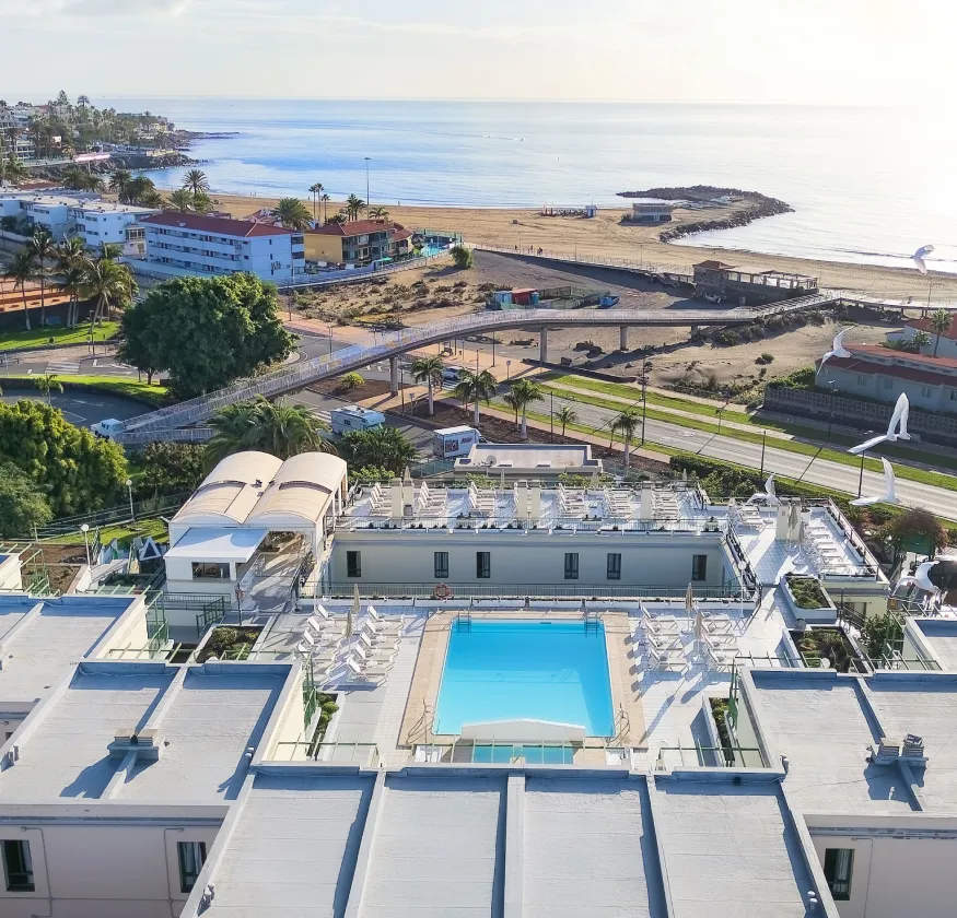 Vista a&eacute;rea de un complejo con piscina cerca del mar y una playa al fondo.