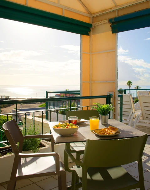 Terraza con mesa servida y vista al mar al atardecer.