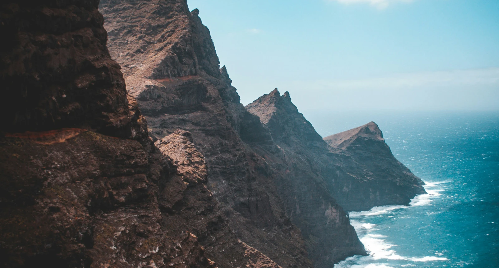 Acantilados rocosos con olas rompiendo bajo un cielo despejado.
