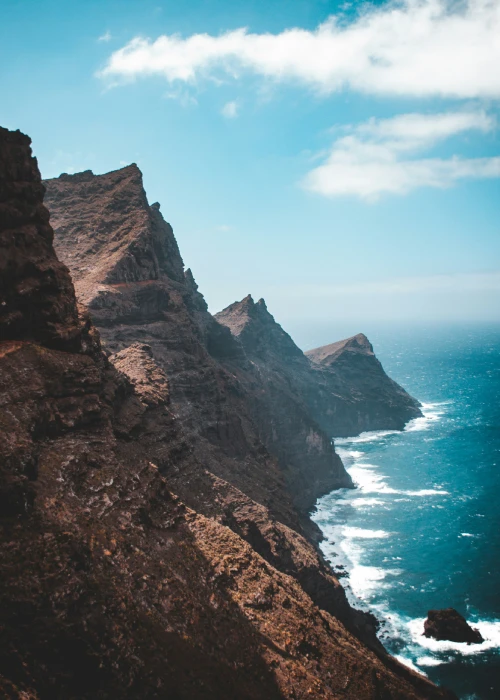 Acantilado rocoso junto al mar bajo un cielo azul con algunas nubes.