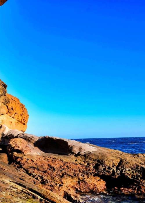 Rocas costeras junto al mar bajo un cielo azul despejado.